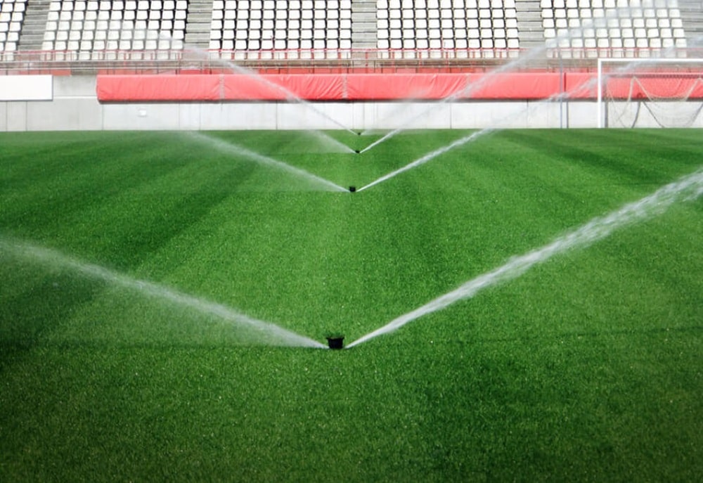 Automatické zavlažování trávníku na fotbalovém stadionu s výsuvnými postřikovači zajišťující rovnoměrnou závlahu pro optimální kvalitu hrací plochy.
